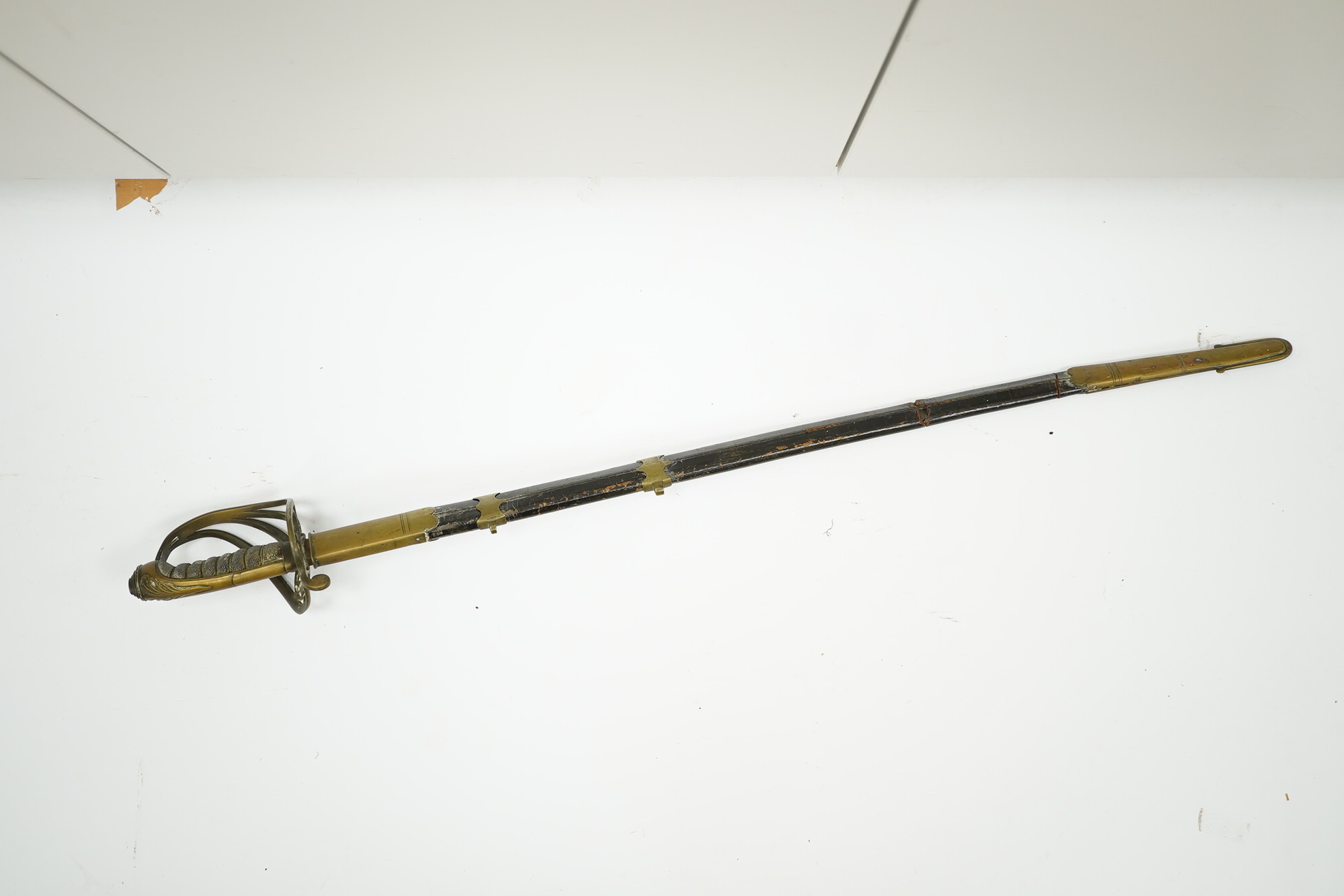 An 1845 pattern infantry officer’s sword, with plain slightly curved blade, regulation solid brass guard, and wire bound fish covered grip, in its brass mounted leather scabbard. Condition - poor to fair, blade cleaned b